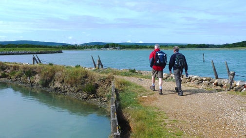 Two walkers stride out along the harbour wall at Newtown with water on both sides